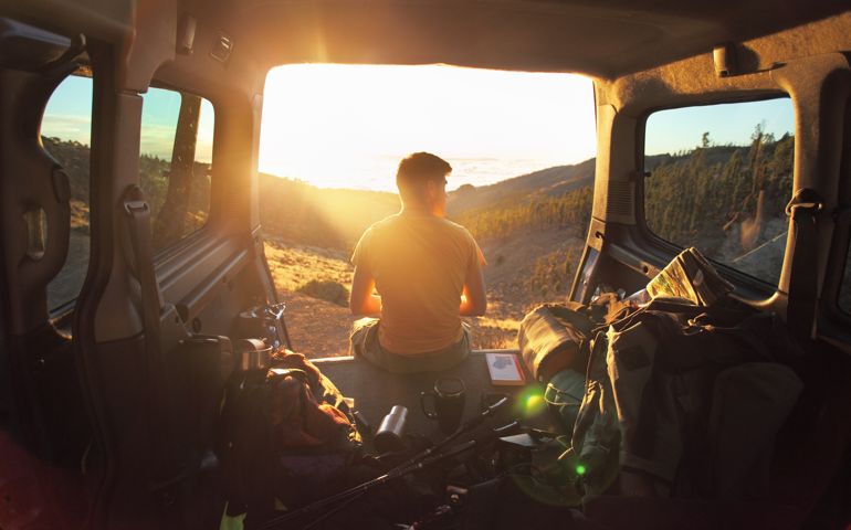 Man sitting in car looking at sunset in mountains