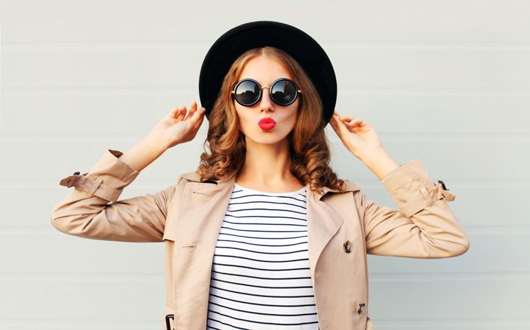 Fashion portrait pretty sweet young woman blowing red lips wearing a black hat sunglasses coat over grey background