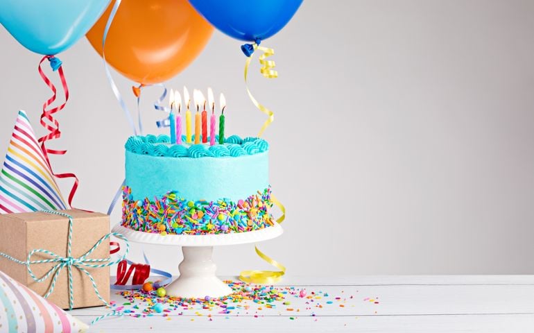 Blue Birthday cake, presents, hats and colorful balloons over light grey.