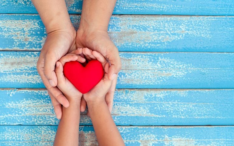 Red heart in child kid and mother hands on old blue wooden table in vintage retro style