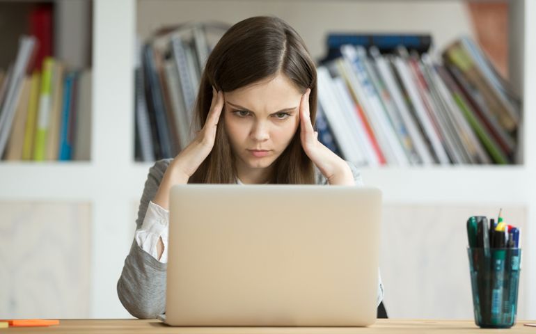 Focused concerned student learning difficult homework assignment with laptop online,