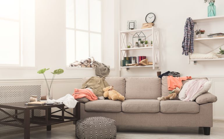 Sofa in messy living room with many stack of clothes. Disorder and mess at home
