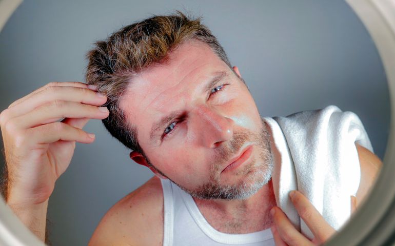 worried and concerned man looking at bathroom mirror finding gray hair frustrated in unhappy aging