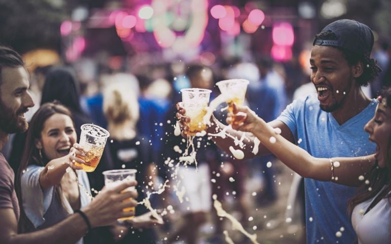 Young happy friends having fun while toasting and spilling beer on a music festival.