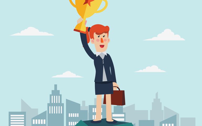 Successful, smiling, young, happy business woman standing on a top of a mountain and holding up winning trophy