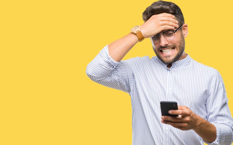 Young handsome man texting using smartphone over isolated background stressed with hand on head, shocked with shame and surprise face, angry and frustrated.