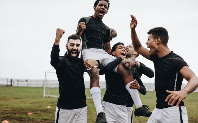 Soccer players celebrating success by lifting a teammate on shoulders