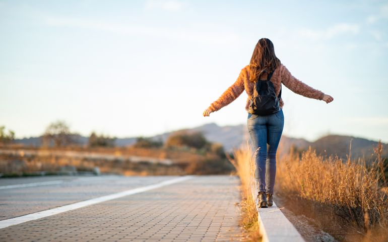 Beautiful woman walking and balancing on street curb or curbstone during sunset