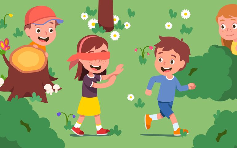 Boys, girls kids playing hide and seek on beautiful summer lawn. Blindfolded girl seeking friends hiding behind bushes, trees.