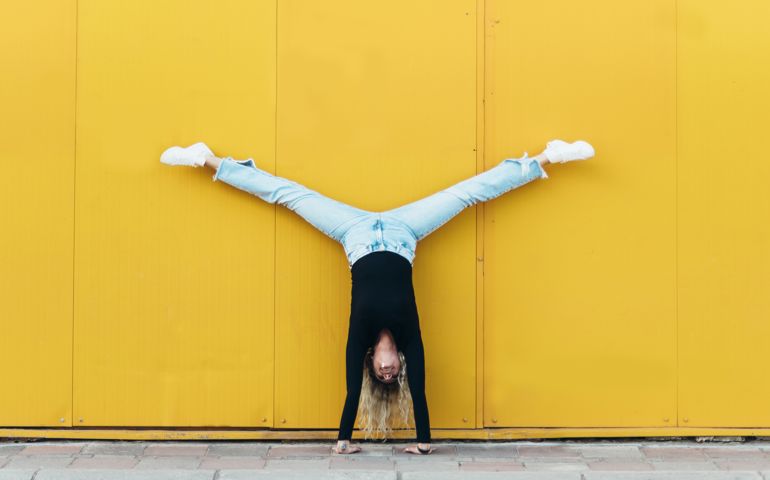 Woman doing hand stand while in front of the yellow wall
