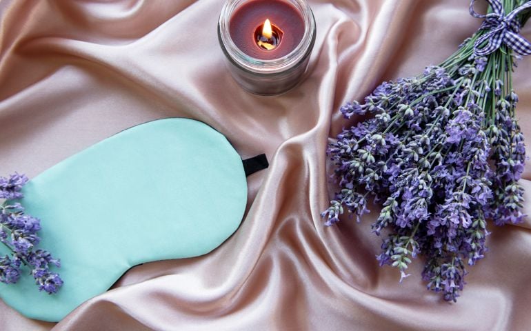 Healthy sleep concept. Lavender bouquet, sleep mask and candle on silk background