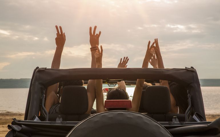 Back view of a group of happy friends sitting in a car with hands raised and having fun