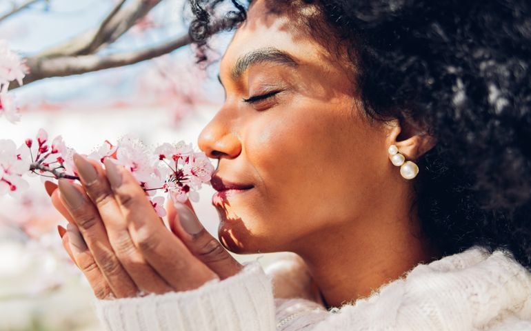 Beautiful woman smelling the soft, fresh and natural scent of pink flowers in spring in bloom.