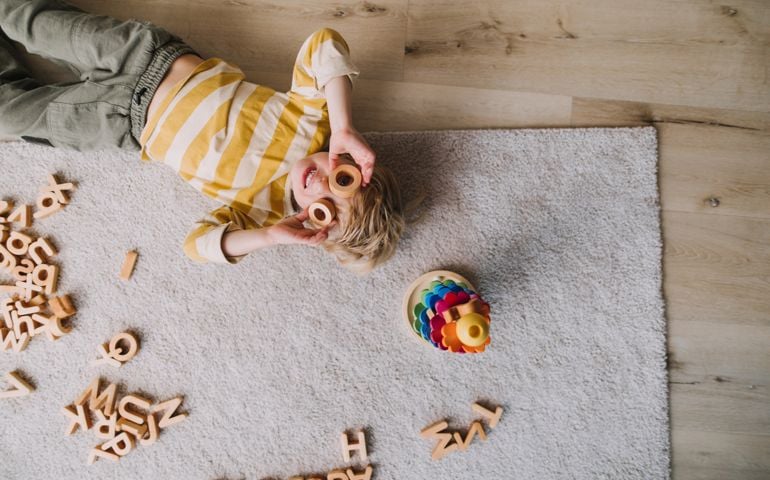 Overhead view of cheerful small boy playing with wooden toys at home.