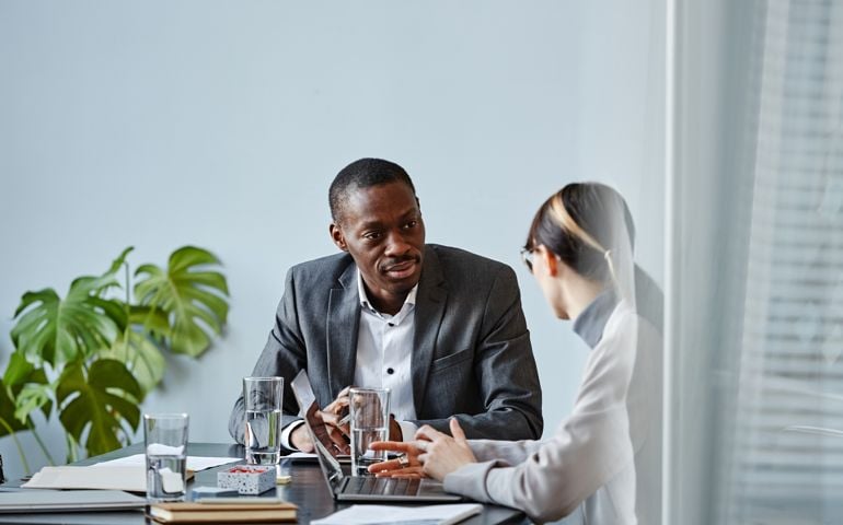 Portrait of businessman talking to female colleague during meeting in office against pale blue wall,