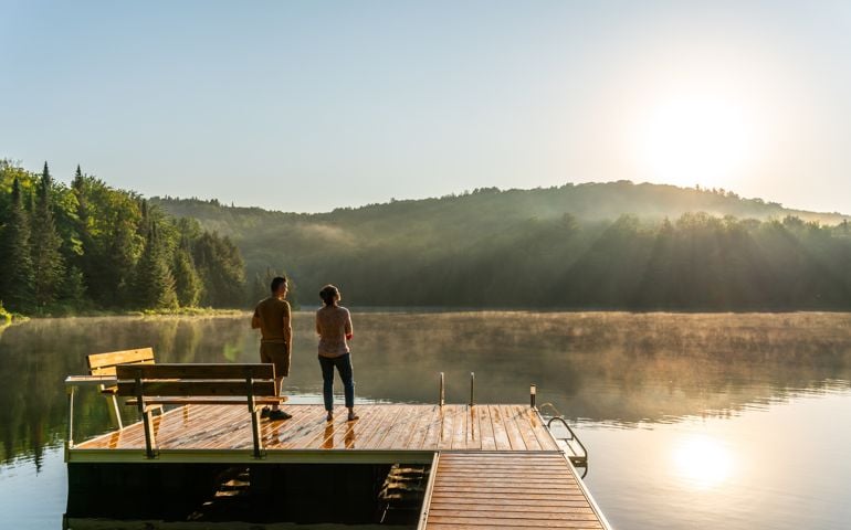 A couple relaxing by a small and quiet fishing lake in the Laurentides (Laurentians), Quebec, during a sunrise of summer.