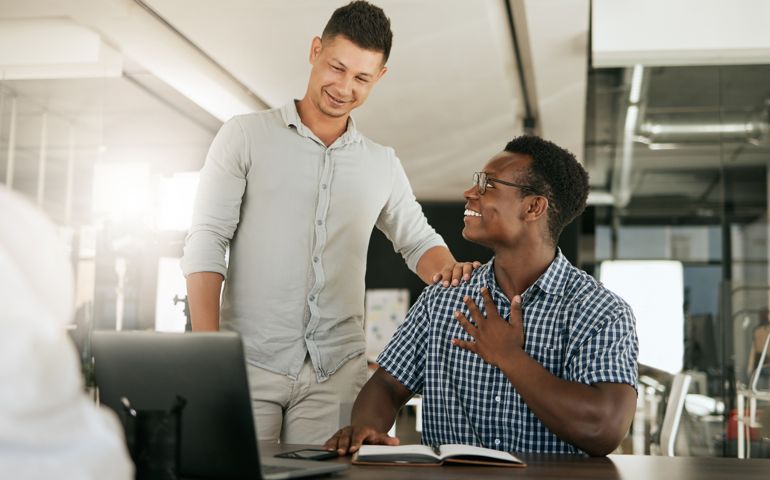 Two diverse businessmen talking at a desk discussing new project on laptop.