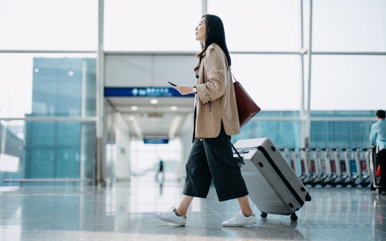 woman carrying suitcase and holding smartphone on hand,
