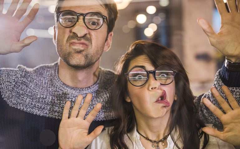 Playful colleagues having fun while sticking their faces on glass wall.