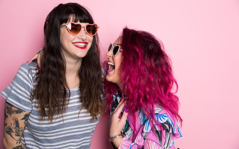 Two woman laughing against a pink back ground