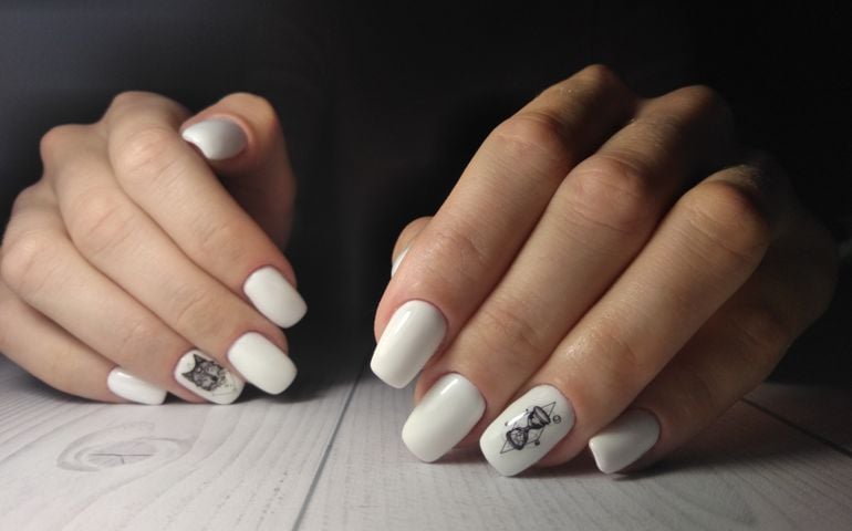 White nail cover with black wolf design and geometry on dark background.