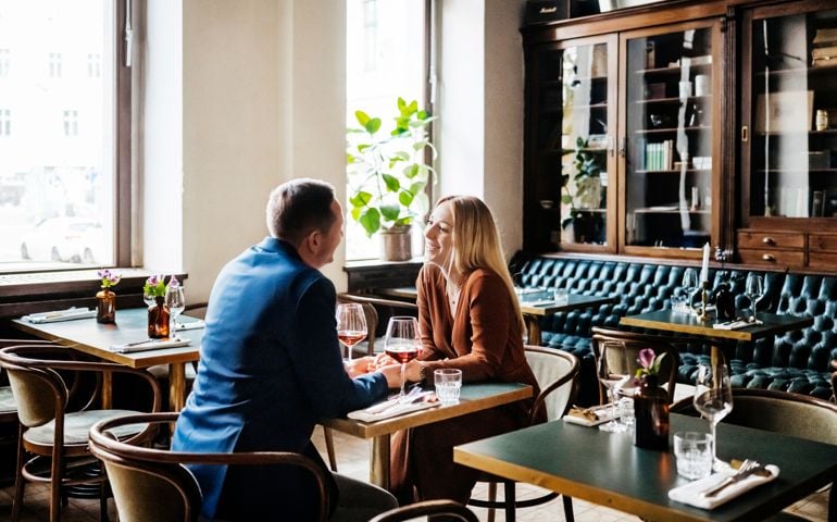 A couple holding hands while sitting down at a table and drinking red wine in a restaurant for lunch together,
