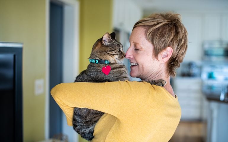 A pretty middle aged woman holds her tabby cat in her home.