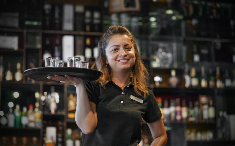 Waitress carries a whiskey glass on a tray in hotel restaurant, bar.