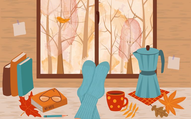 Feet in knitted socks are lying on the table. Outside the window is an autumn landscape.