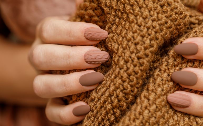 Women's hands with fashionable manicure with a knitted texture on the background of a knitted scarf or plaid.