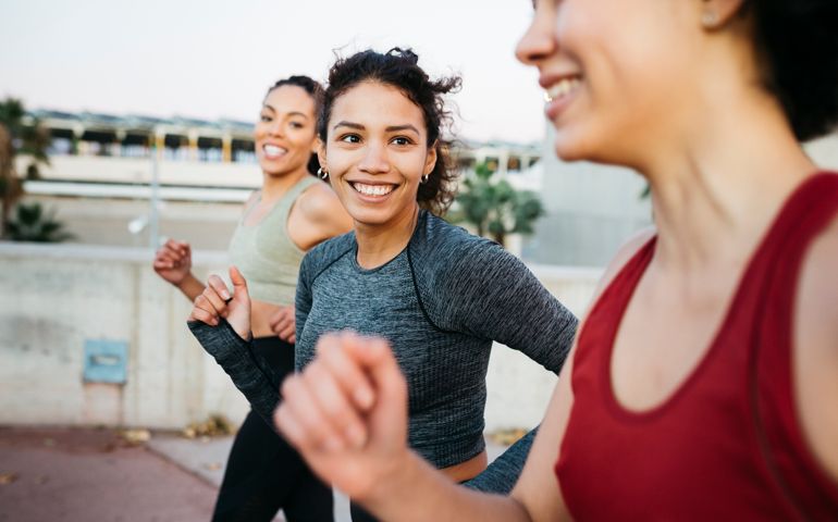 Three smiling young women, wearing sports clothes, jogging on an urban scenario