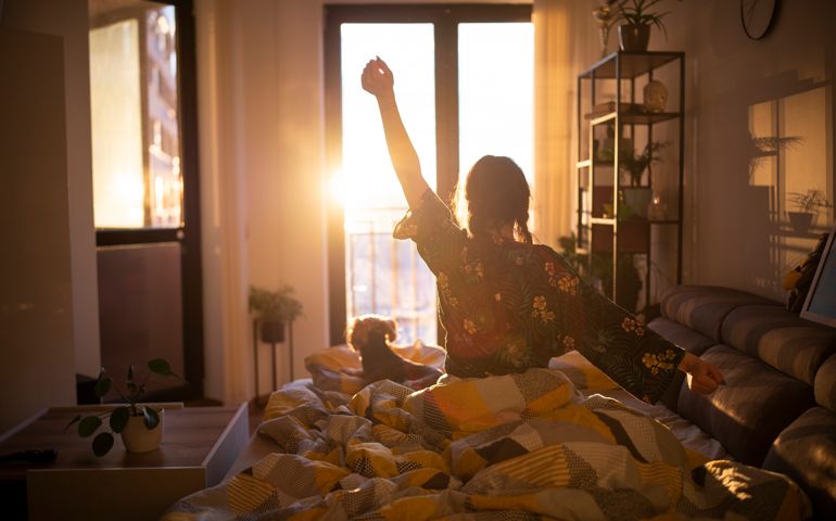 Young woman streching in bed in the morning while looking at the sunrise.