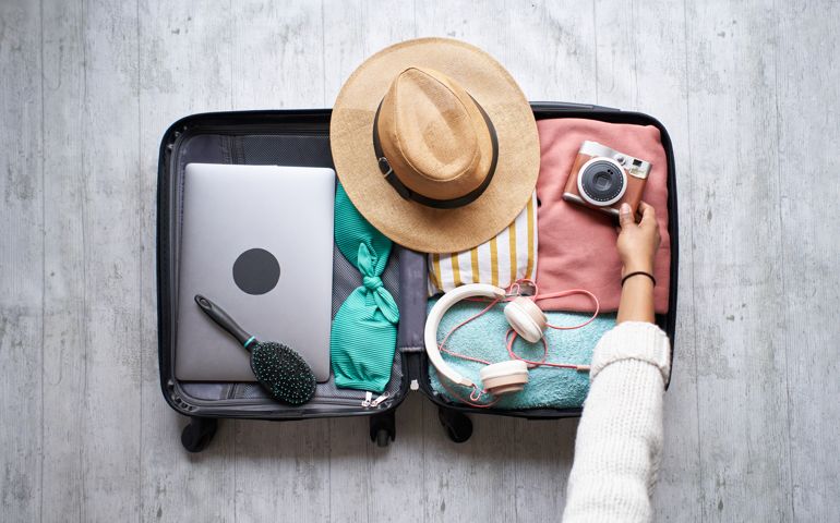 Photo of an open luggage for summer travel with an unreasonable black woman packing beach items.