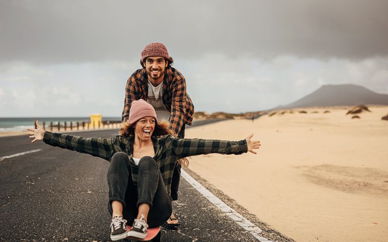 Couple having fun with skateboard on the road near the sea