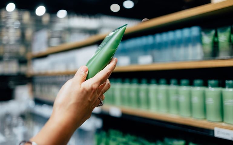 A cropped photo of an woman holding a tube of a hand cream while shopping at a store.