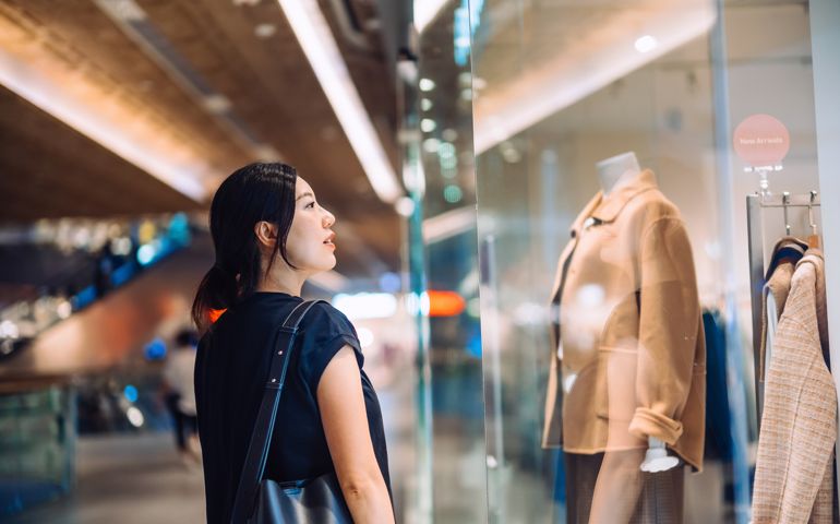 woman standing outside a boutique looking at window display while shopping in shopping mall