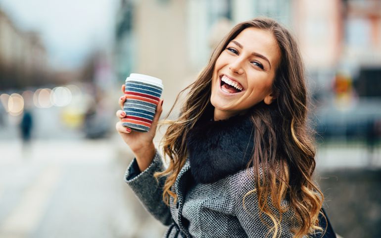Young woman with coffee cup smiling outdoors