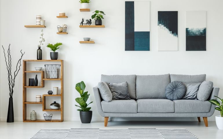 Elegant living room interior with a grey sofa, wooden shelves, plants and paintings on the wall