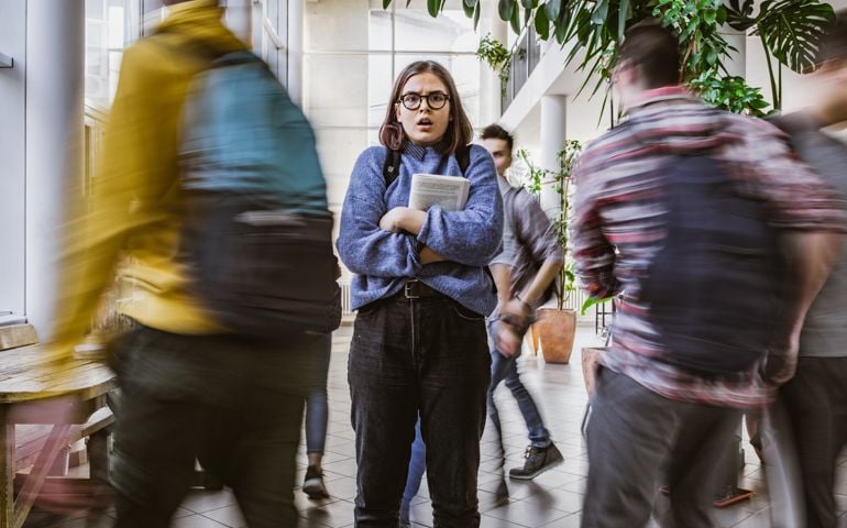 Shocked nerdy student among her classmate in blurred motion.