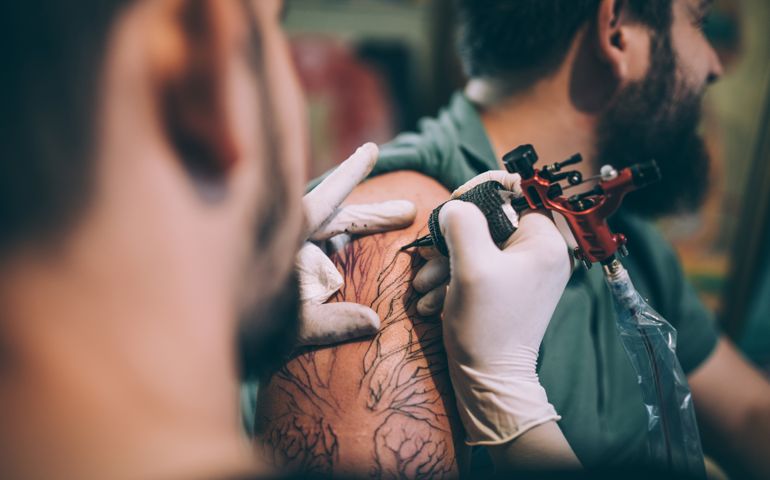 Two men, tattoo artist tattooing a man's arm in his tattoo studio.