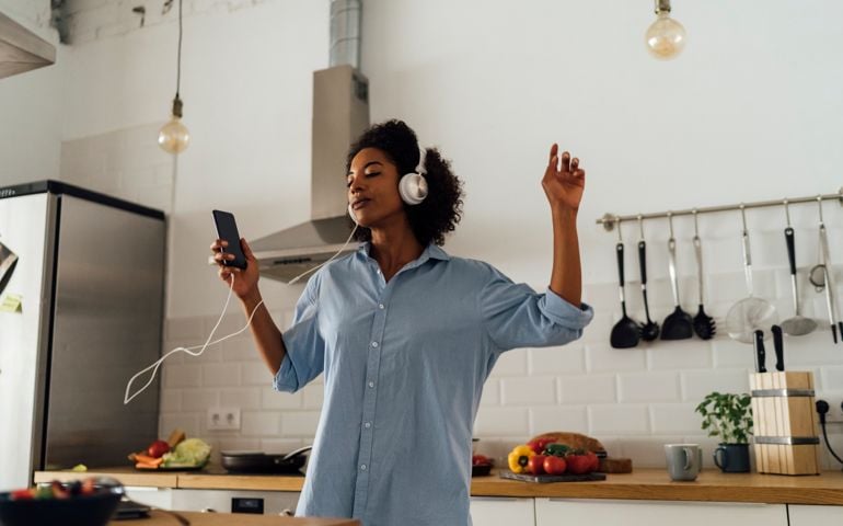 Woman dancing and listening music in the morning in her kitchen