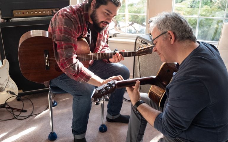 Young Man Teaching Mature Caucasian Man to Play Guitar