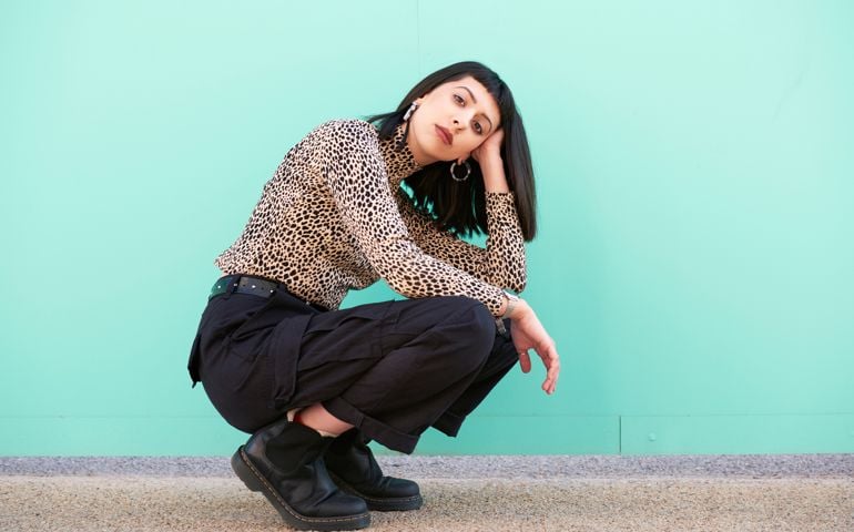 Young woman crouching down in front of blue wall.
