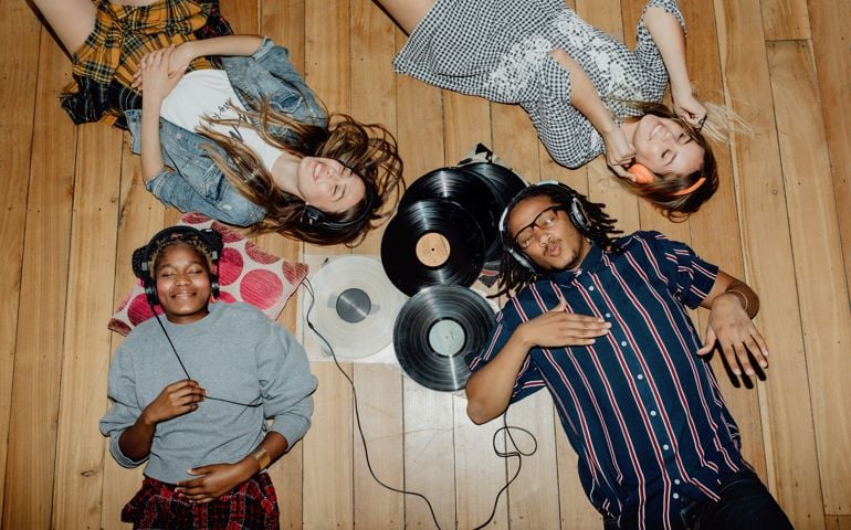 Group of young friends listening to music with vinyls scattered about