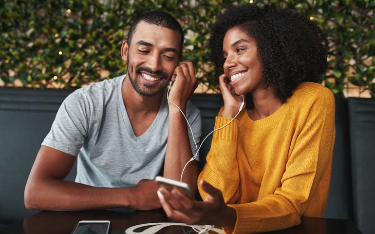 portrait of an couple together listening music in cafe on one earphone