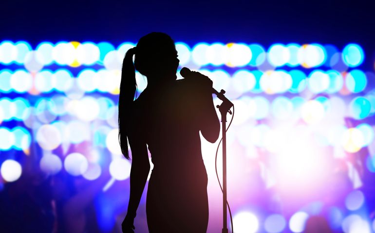 Silhouette of woman with microphone singing on concert stage in front of crowd