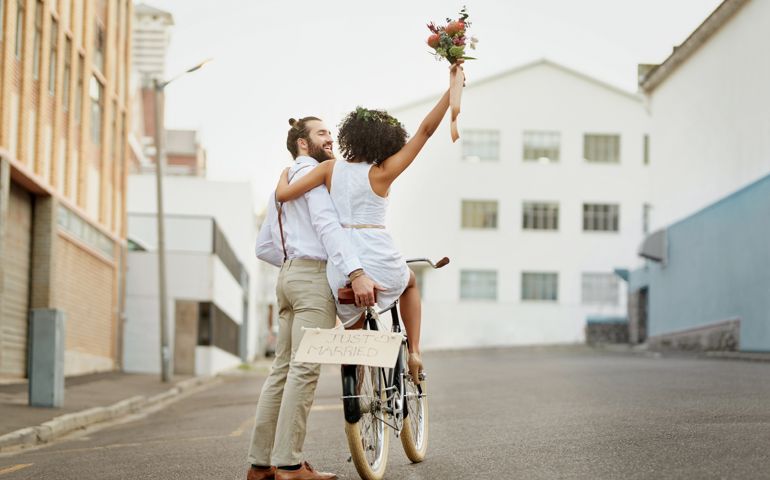 Shot of a newly married young couple riding a bicycle through the city