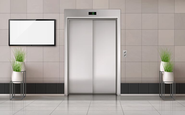 Office hallway with closed elevator door and TV screen on the wall.