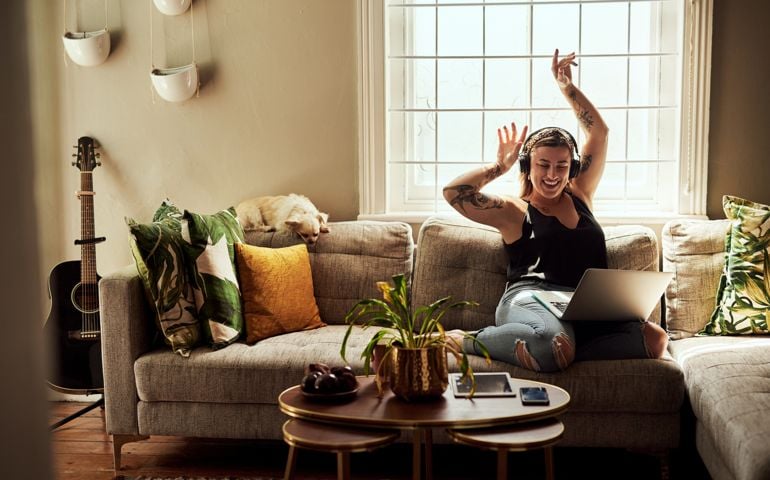 Shot of a young woman using a laptop and headphones on the sofa at home