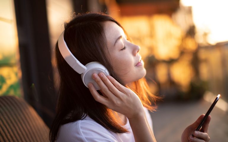 Close-up Shot Of Young Woman Enjoying Music Over Headphones And Using Smart Phone